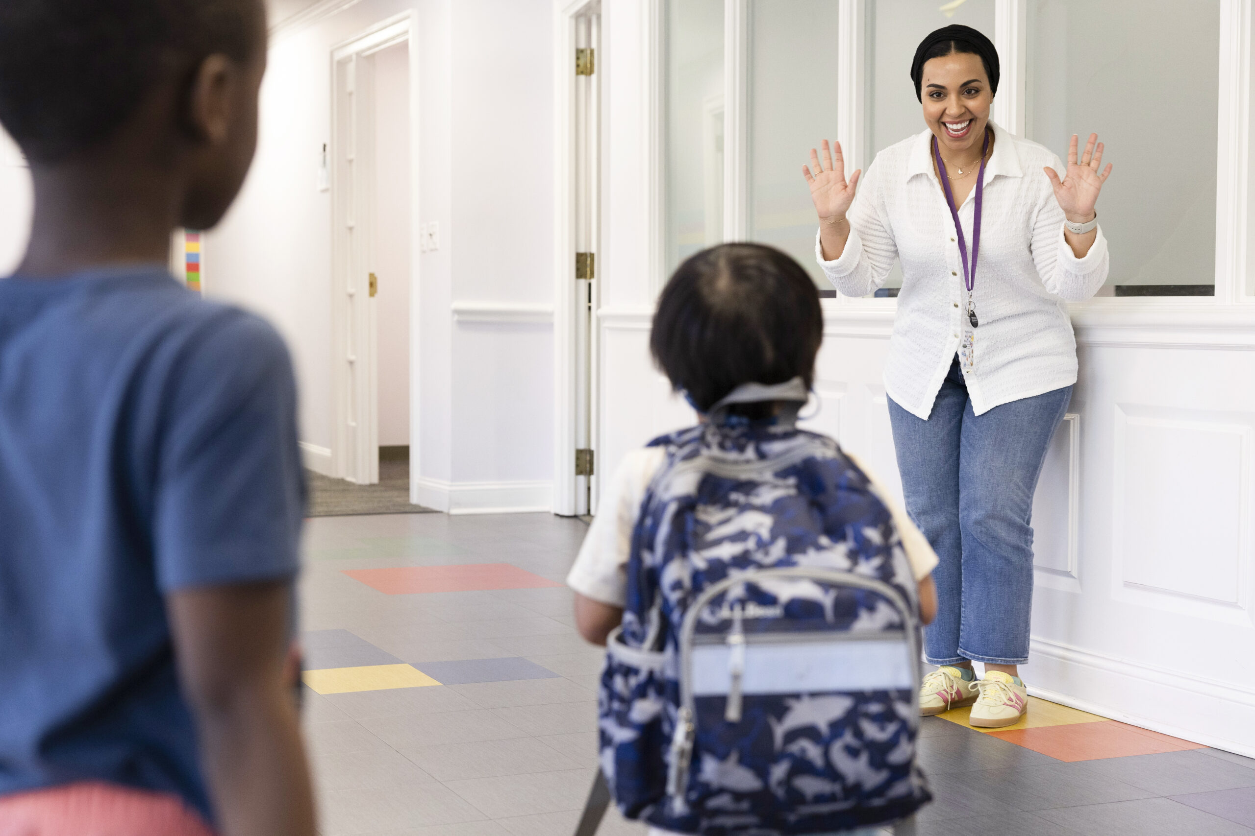 A hispanic woman greeting a young boy with black hair, with a dark skin boy watching.